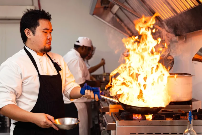 A chef flambéing a pan at the stove in a professional kitchen