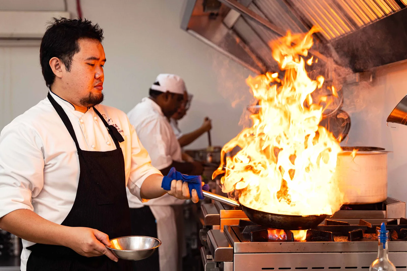 A chef flambéing a pan at the stove in a professional kitchen